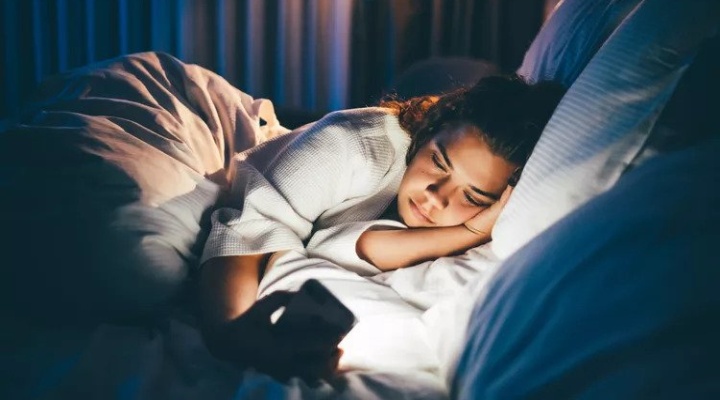 دختری که در رختخواب گوشی به دست دارد