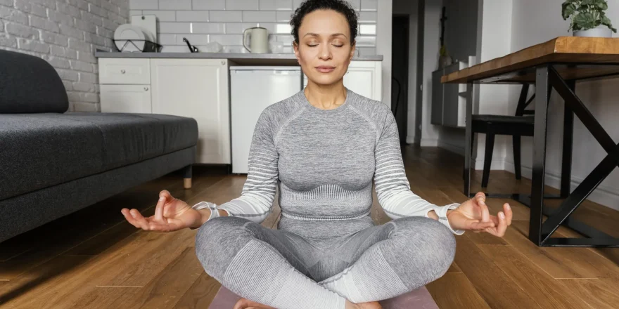 یوگا زن نشسته با لباس اسپرت خاکستری در وسط خانه