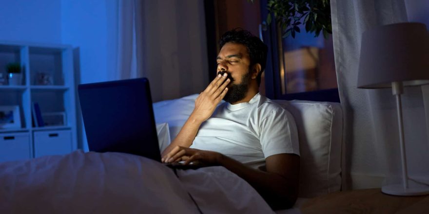 خمیازه مرد در تخت پشت لپتاپ